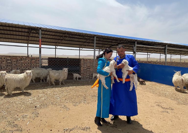 Two herders in traditional dress tending goats in a barn